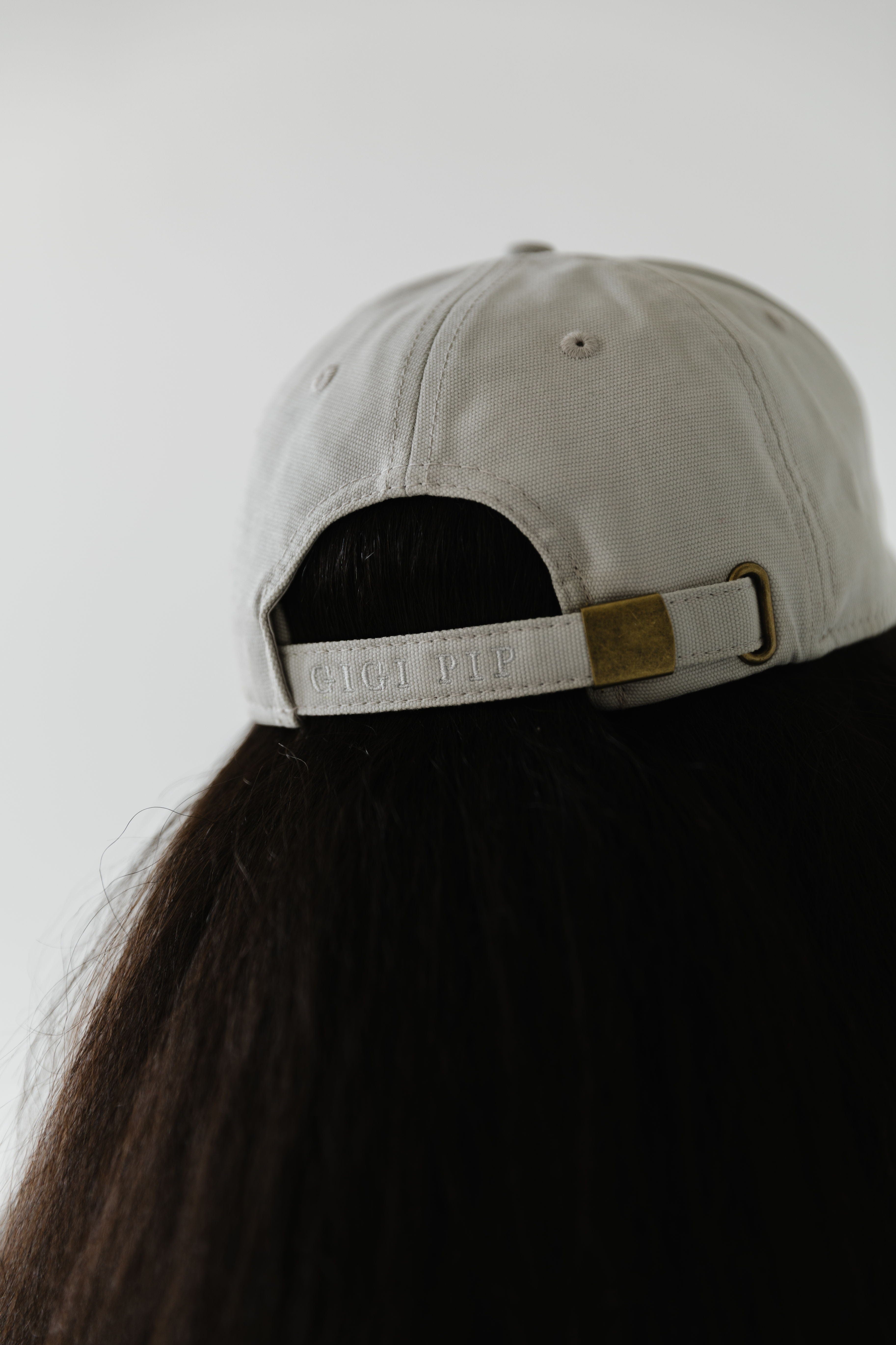 Woman wearing a stone colored ball cap facing behind against a plain background #color_stone