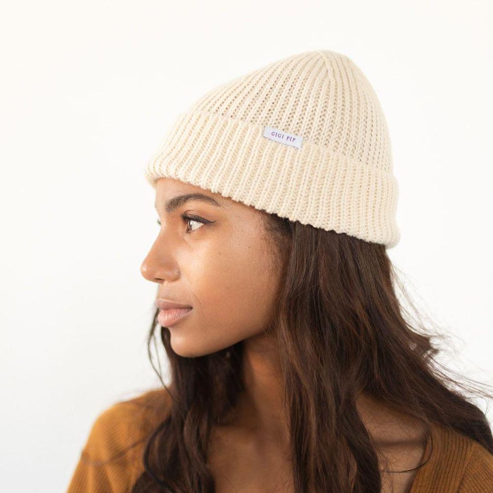 Woman wearing an oatmeal colored knit beanie with the brand label facing sideways against a plain background #color_oatmeal