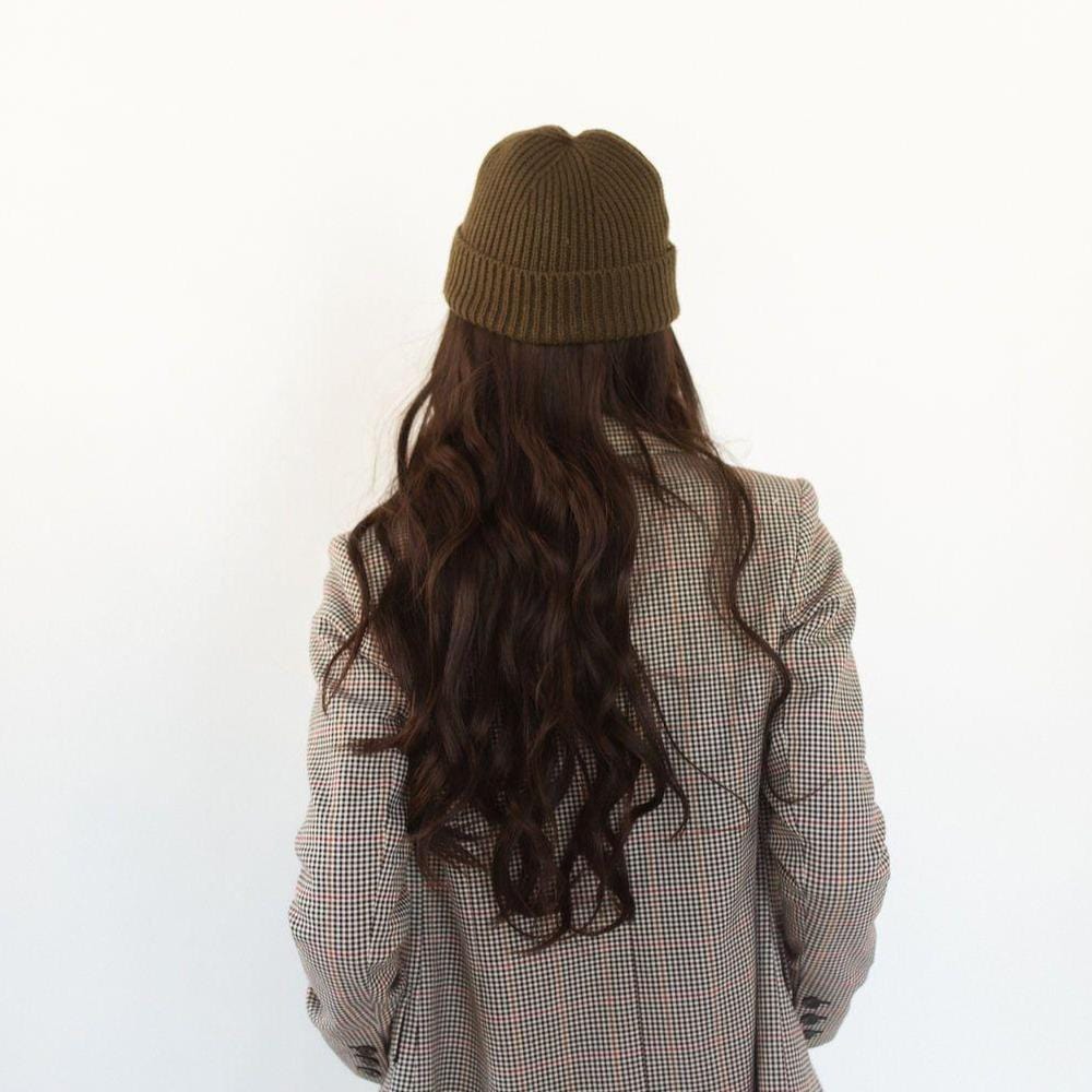 Woman wearing an olive colored knit beanie and a blazer, facing behind against a plain background #color_olive