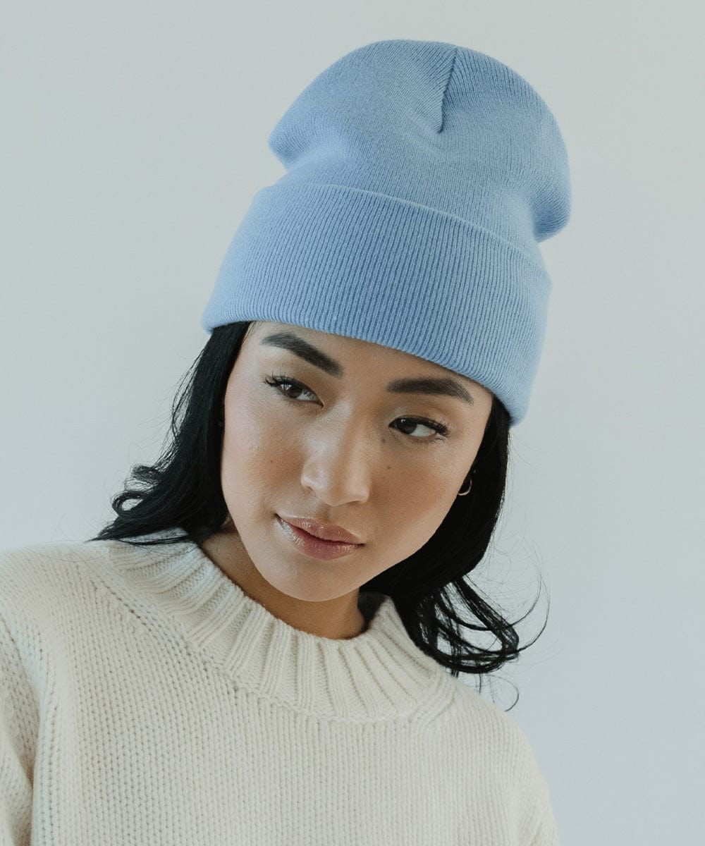 Woman wearing an azure blue colored beanie and a white sweater against a plain background #color_azure blue
