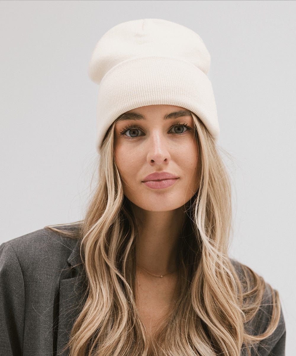 Woman wearing a cream beanie and a grey coat against a plain background #color_cream