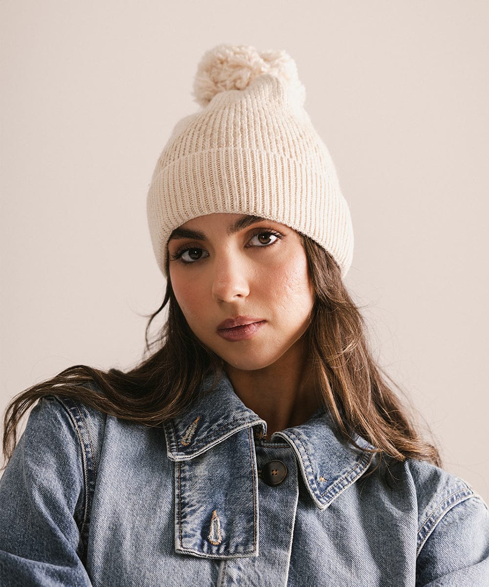 Woman wearing a beige knit beanie with a pom-pom on a plain background #color_cream