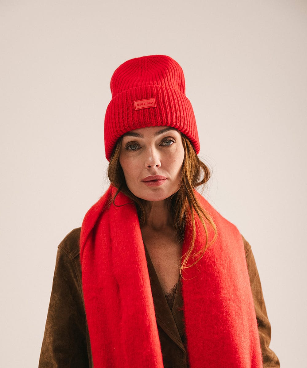 A woman wearing a ruby red colored ribbed beanie and a jacket against a plain background #color_ruby red