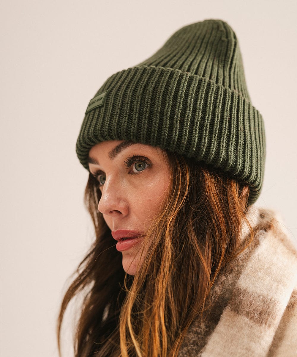 A woman wearing a dark green chunky ribbed beanie, looking sideways against a plain background #color_dark green
