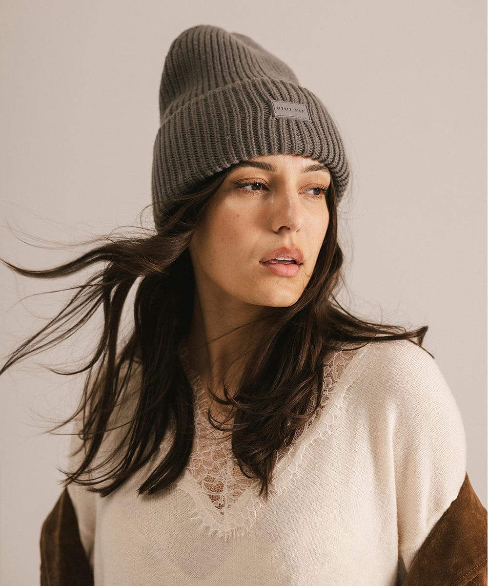 Woman wearing a gray knit beanie with a visible brand logo against a plain background #color_grey