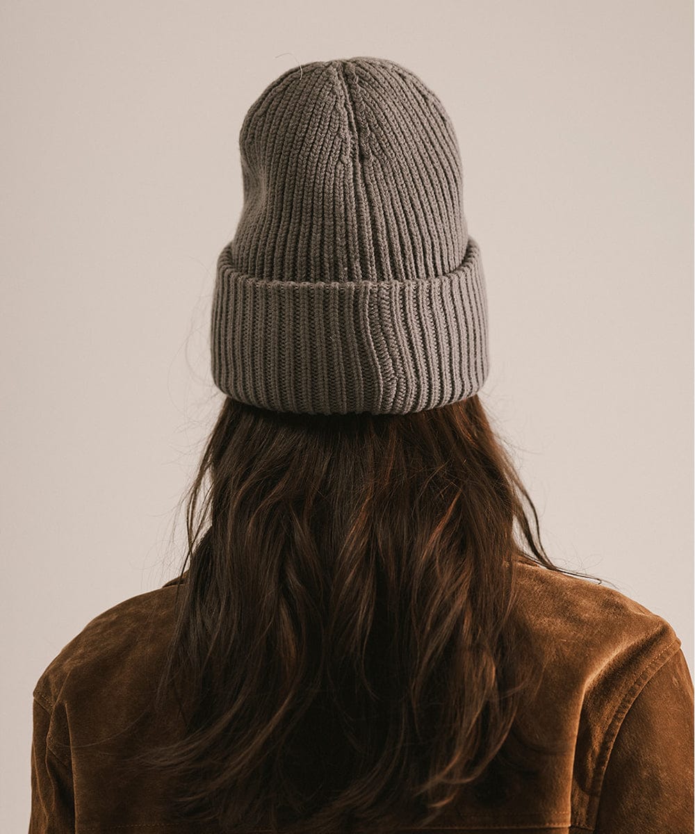 Person wearing a gray knit beanie and brown jacket, facing behind against a plain background #color_grey