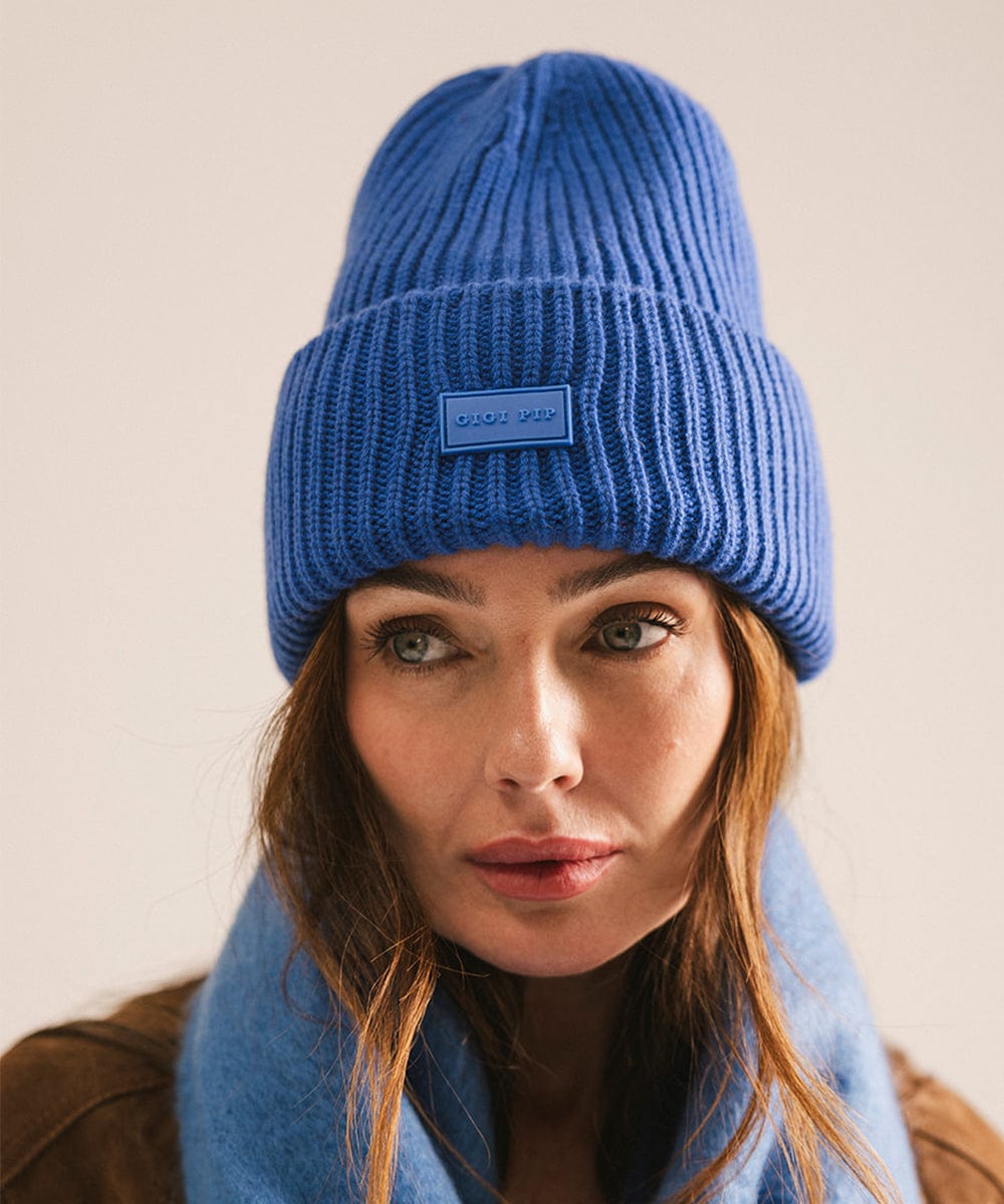 Woman wearing a blue knit beanie and scarf against a beige background #color_alpine blue