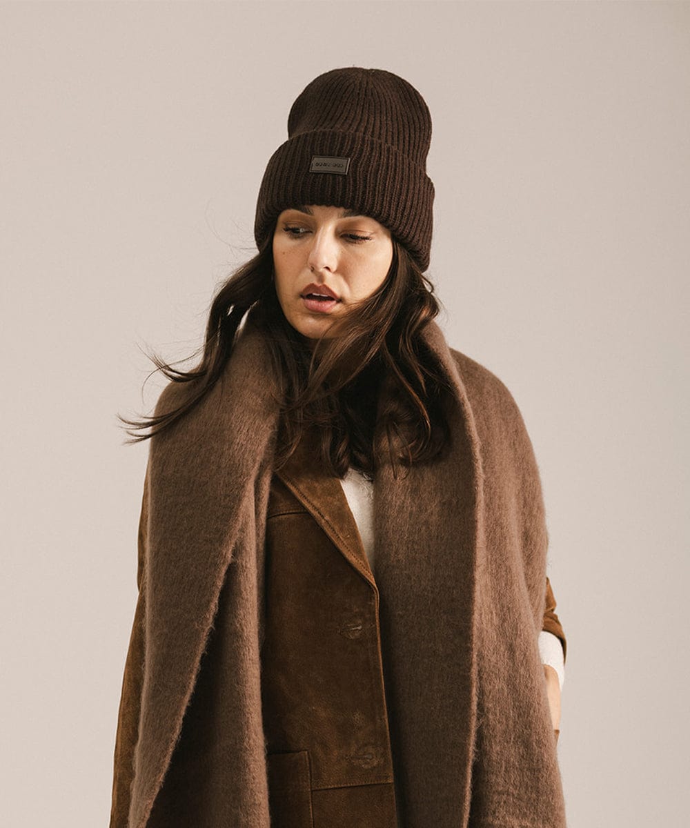 Woman wearing a brown coat and beanie against a plain background #color_dark brown