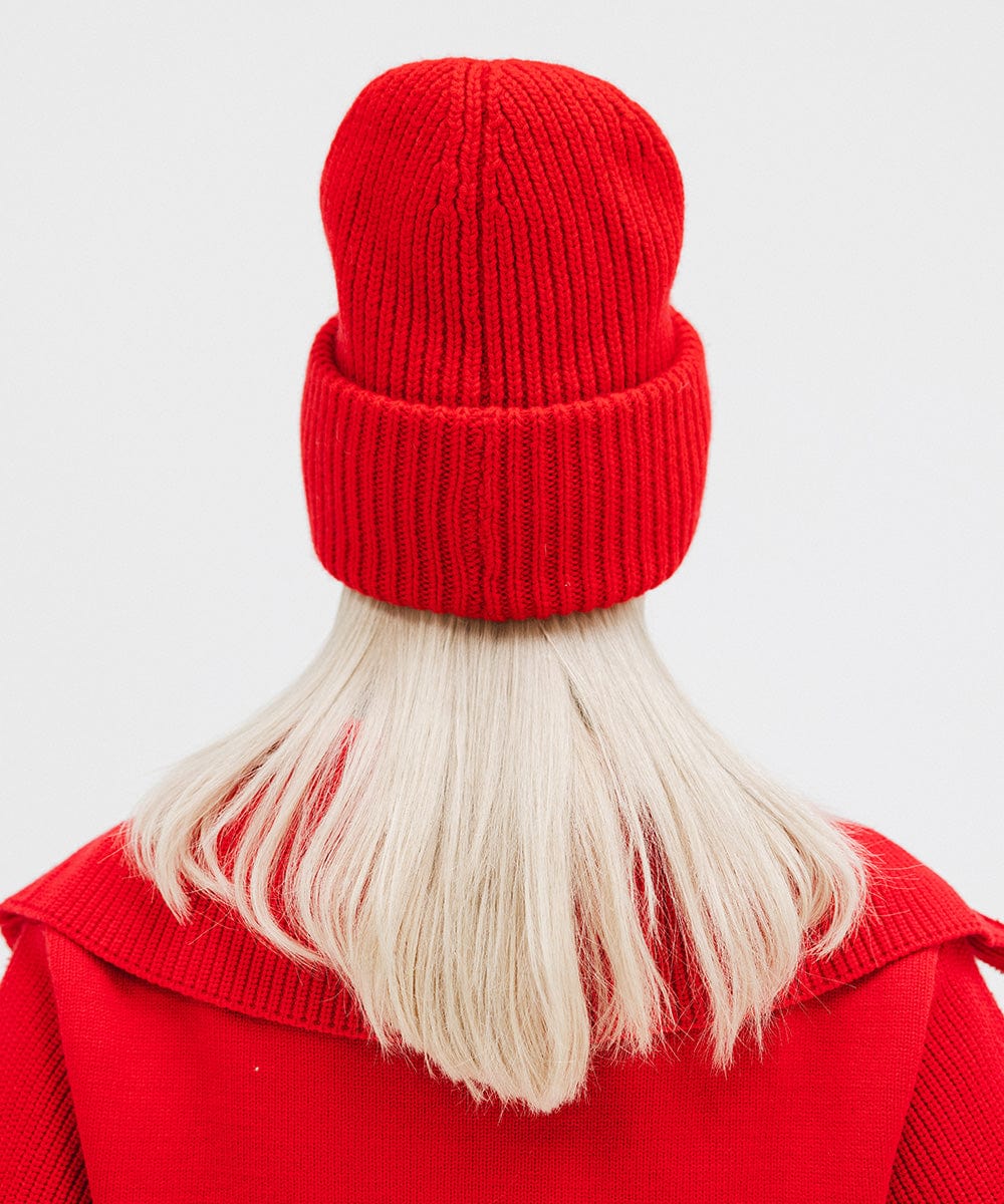 A person wearing a ruby red colored ribbed beanie and a red jacket, facing behind against a plain background #color_ruby red