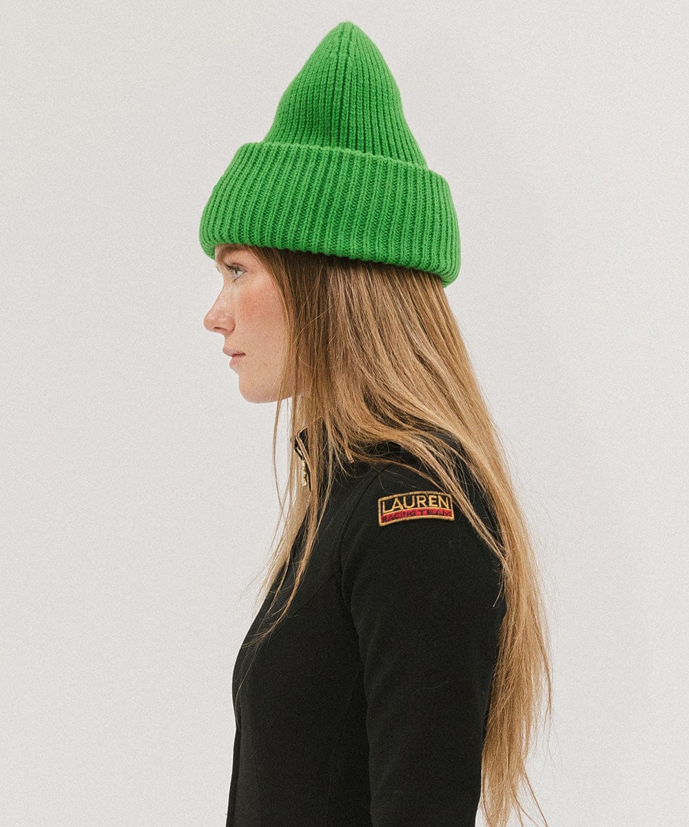 A woman wearing an evergreen colored ribbed beanie and a black jacket, facing sideways against a plain background #color_evergreen