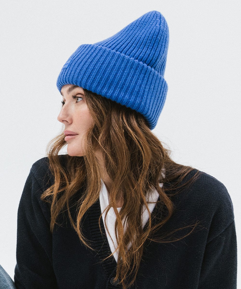 A woman wearing an alpine blue colored ribbed beanie and a dark blue sweater, facing sideways against a plain background #color_alpine blue