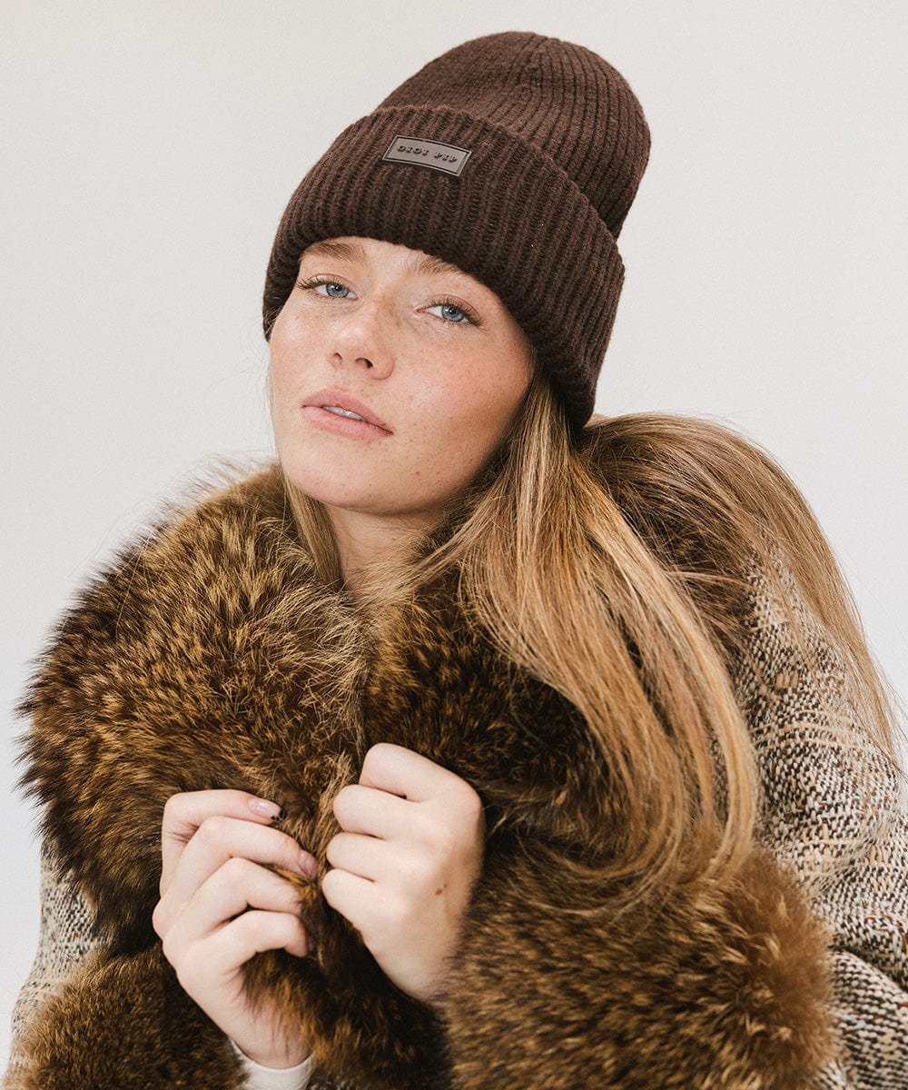 A woman wearing a dark brown chunky ribbed beanie and a brown coat against a plain background #color_dark brown