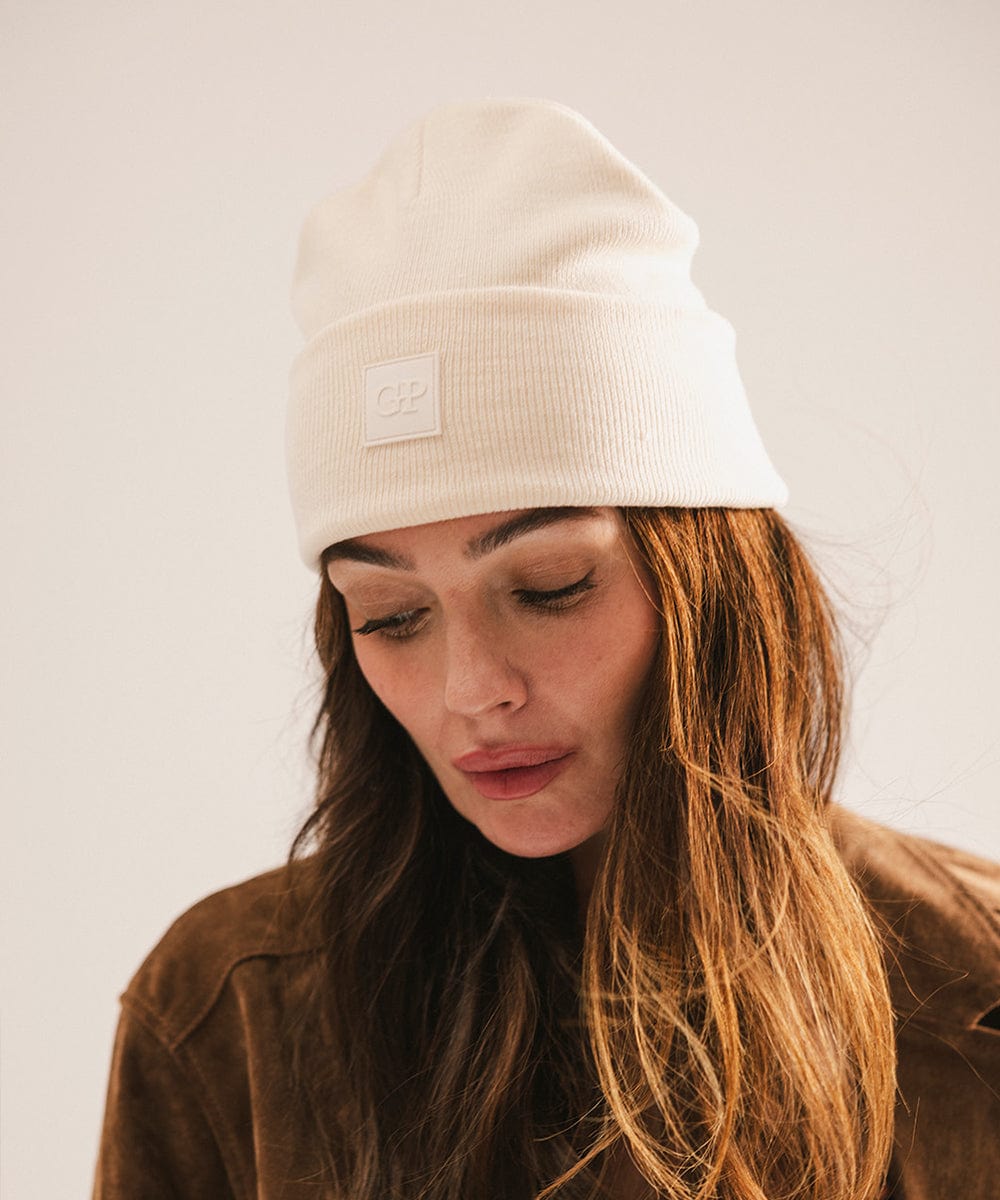 Person wearing an off white beanie with a logo on a plain background #color_off white