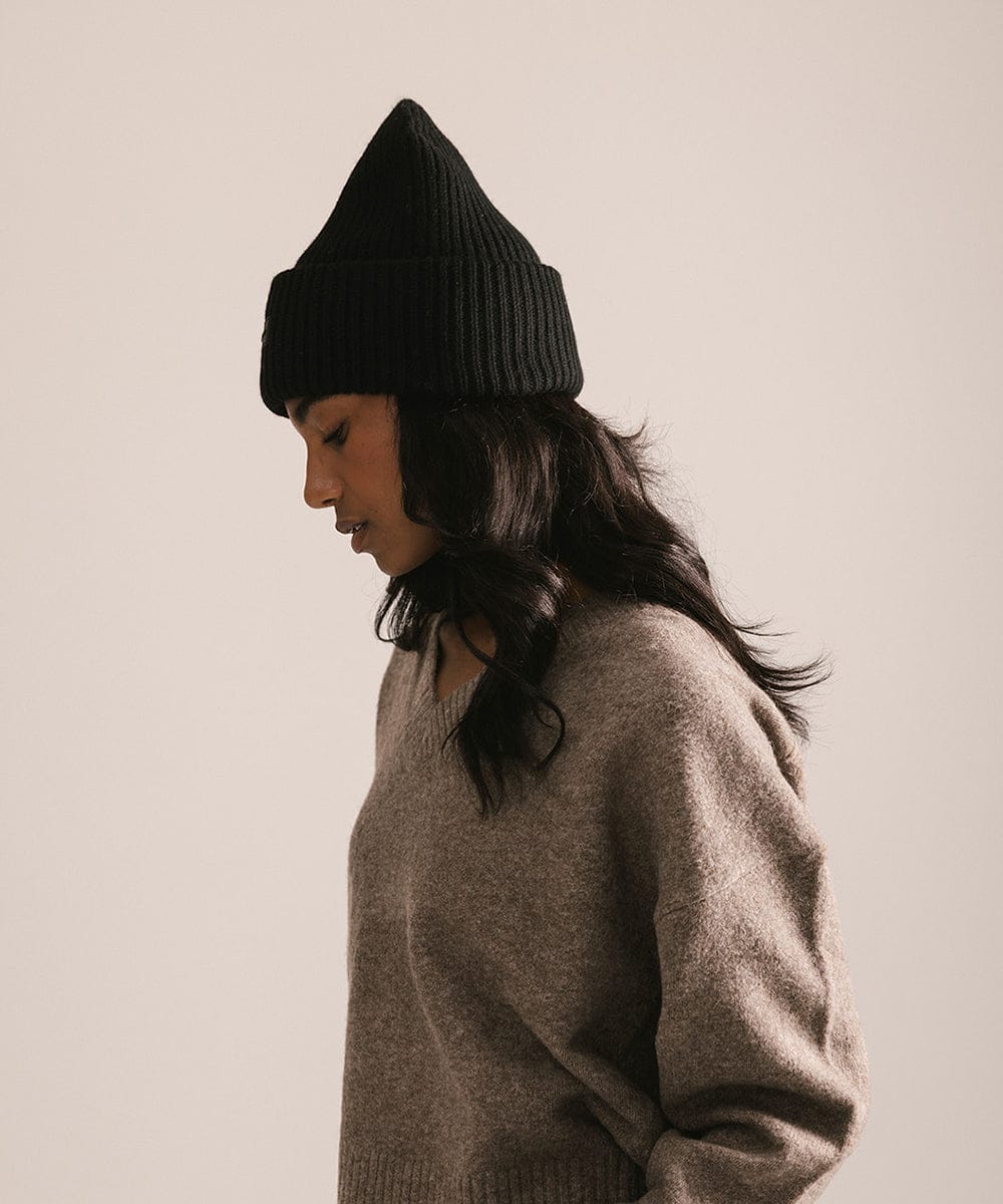 Person wearing a black knit beanie and beige sweater against a plain background #color_black