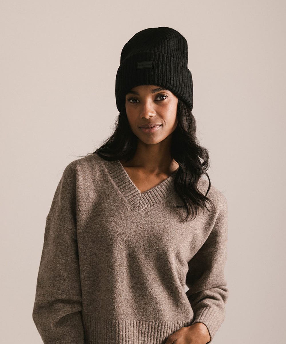 Woman wearing a black beanie and brown sweater against a beige background #color_black