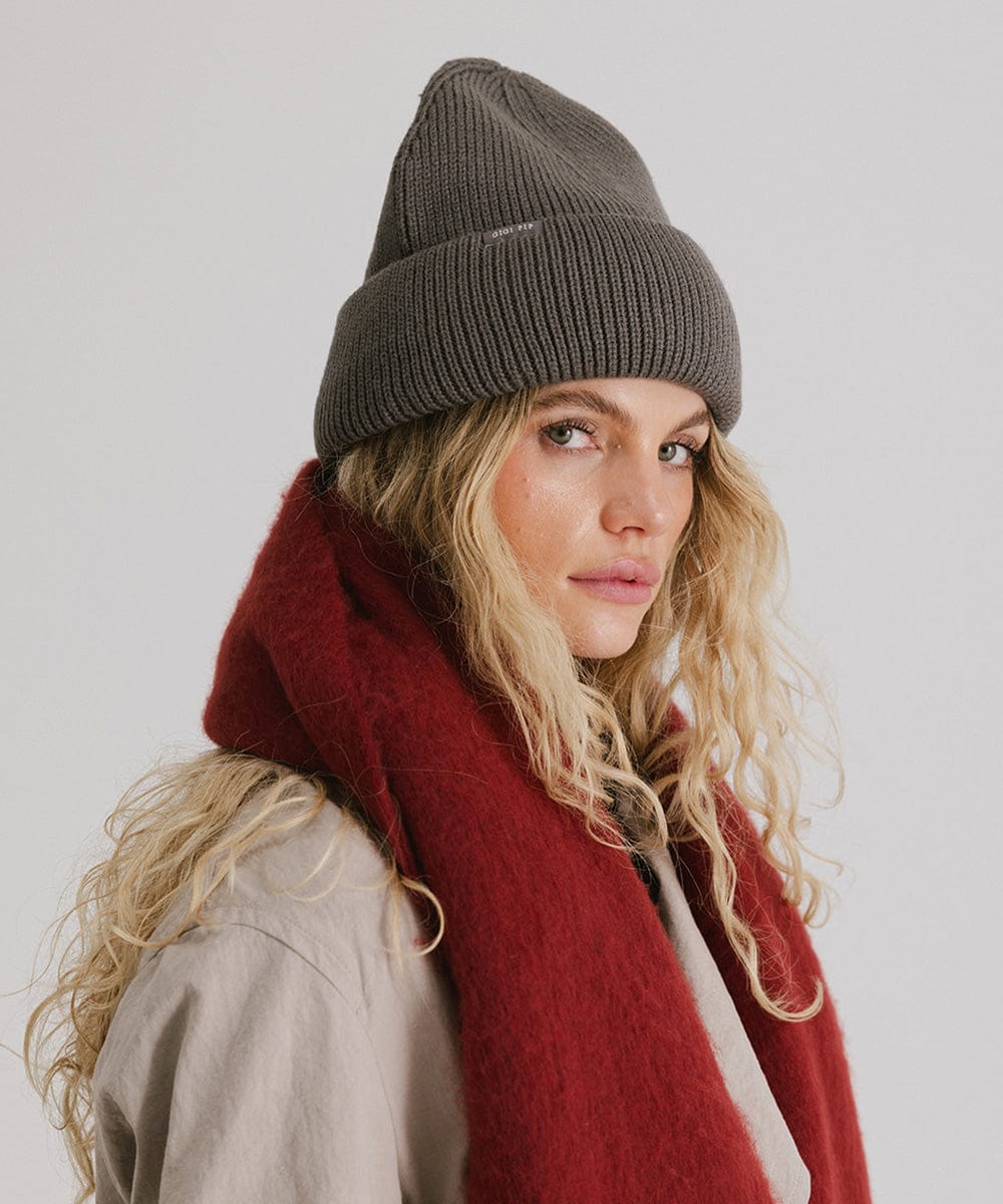 Woman wearing a grey oversized knit beanie and a red oversized scarf against a plain background #color_grey