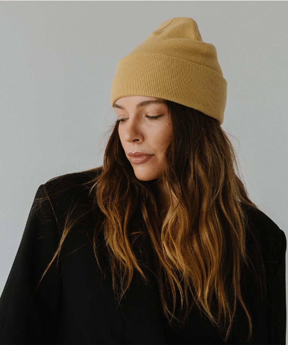 Woman wearing a honeycomb colored beanie and a black coat against a plain background #color_honeycomb