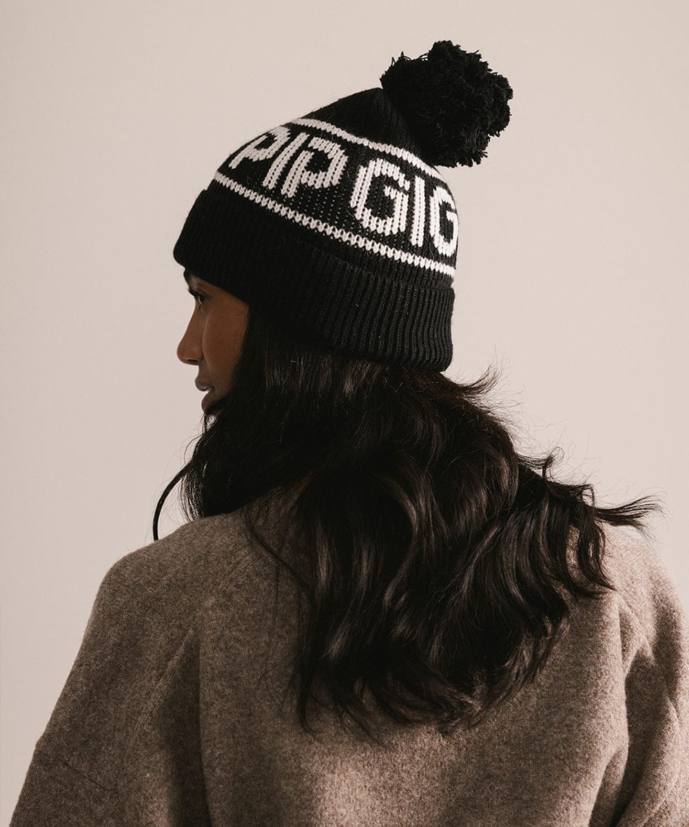 Person wearing a black knit beanie with 'GIGI PIP' branding against a neutral background #color_black