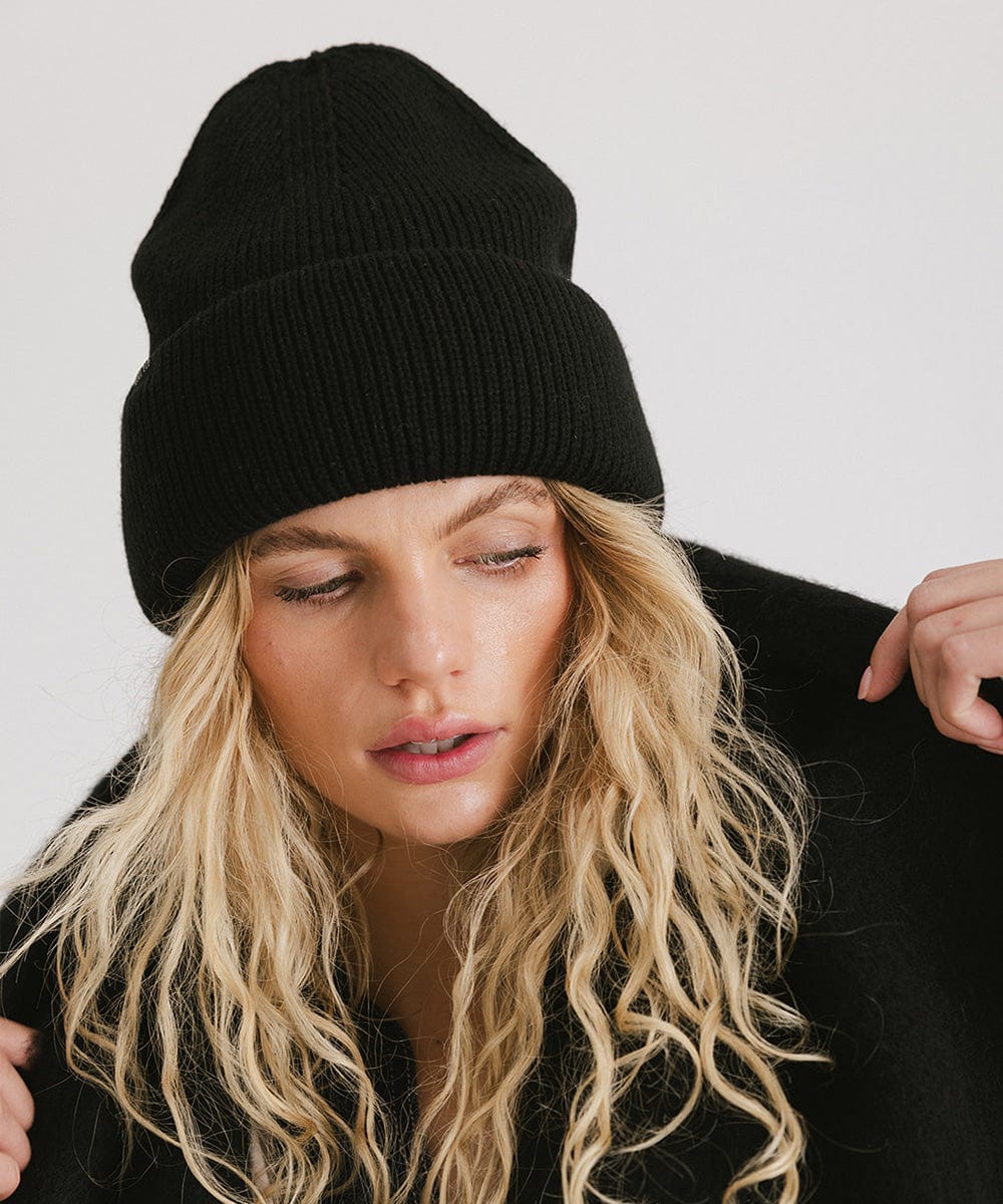 Woman with blonde hair wearing a black oversized knit beanie against a plain background #color_black