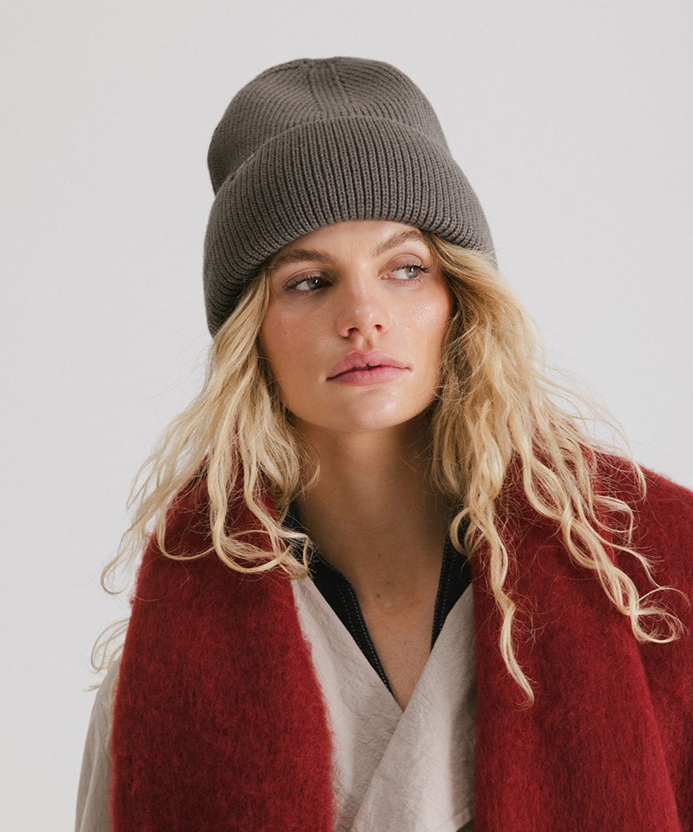 Woman wearing a grey oversized knit beanie and a red oversized scarf against a plain background #color_grey