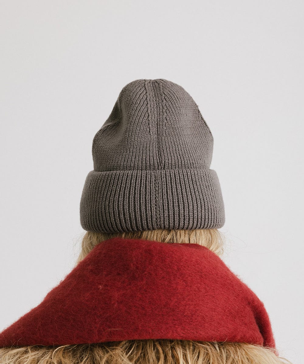 Person wearing a grey oversized knit beanie and a red oversized scarf against a plain background #color_grey