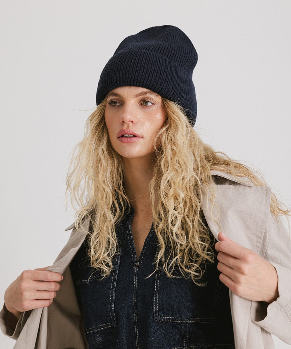 Woman wearing a navy oversized knit beanie and a denim top with a coat against a plain background #color_navy