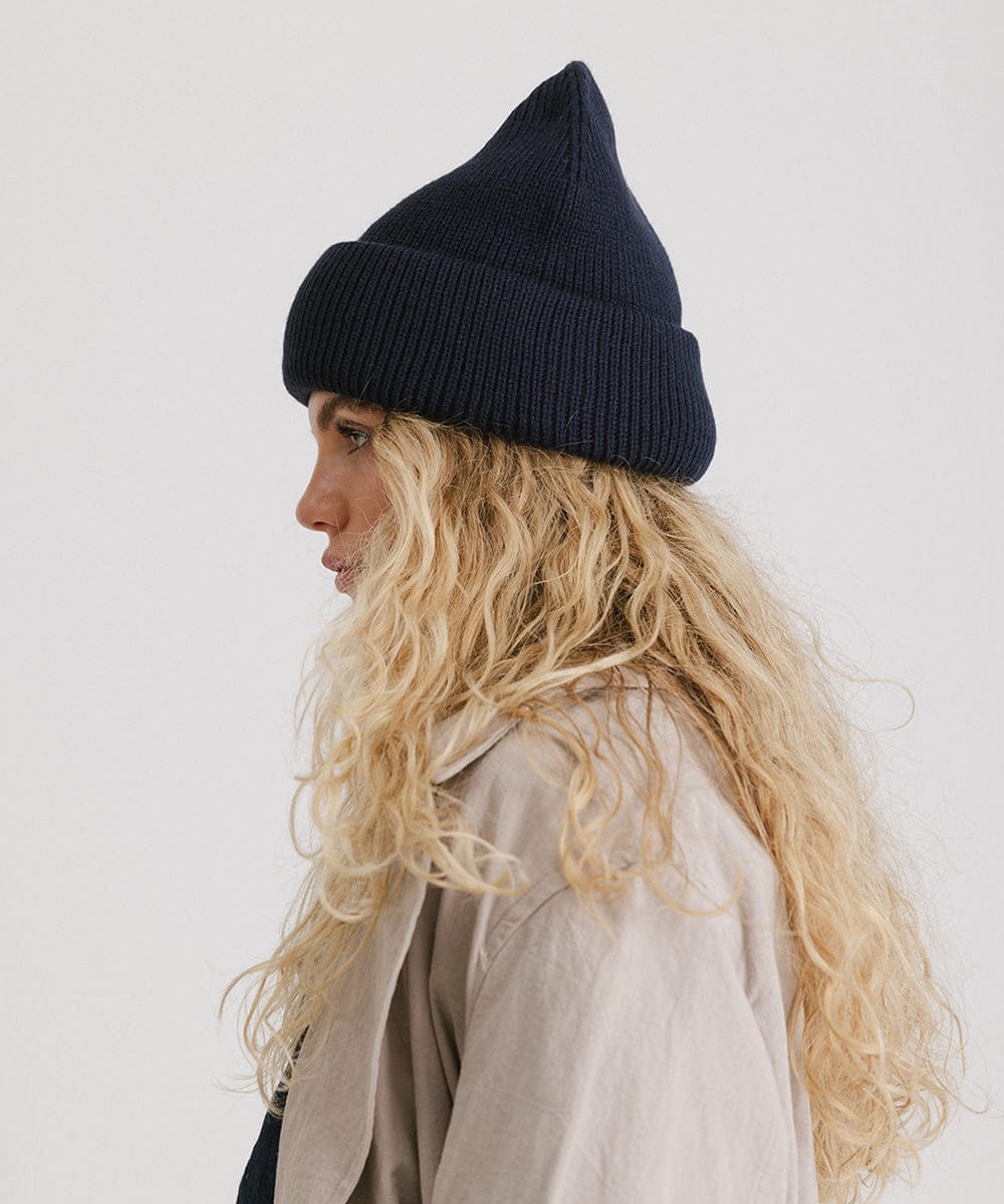 Woman wearing a navy oversized knit beanie and a coat, facing sideways against a plain background #color_navy