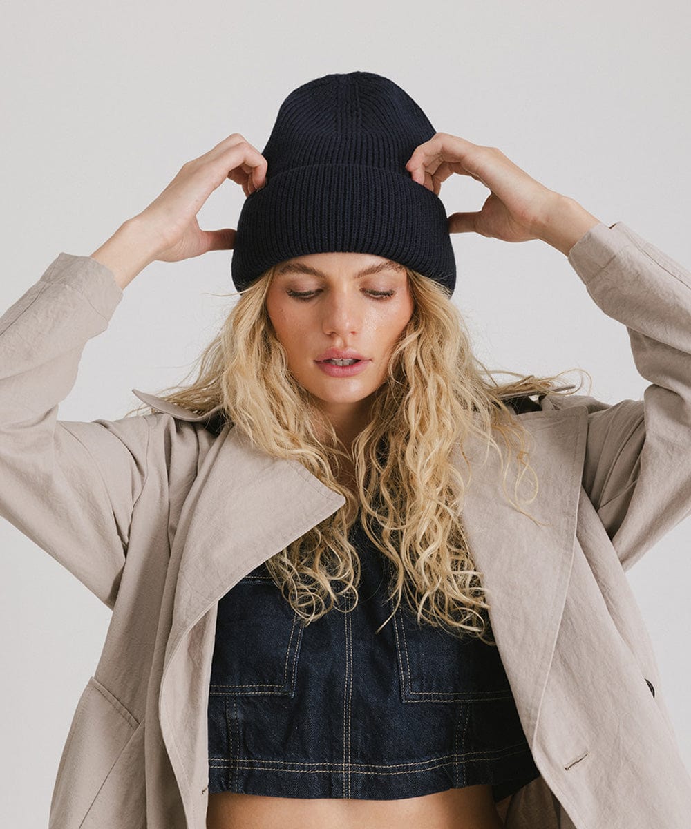 Woman wearing a navy oversized knit beanie and a denim top with a coat against a plain background #color_navy