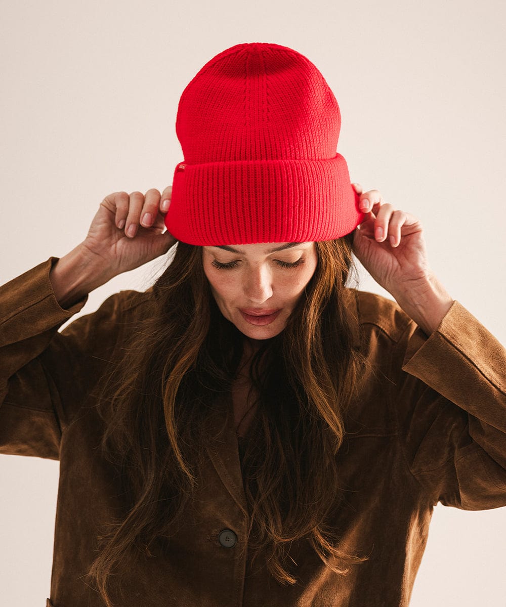 Person wearing a red beanie and brown coat against a plain background #color_red