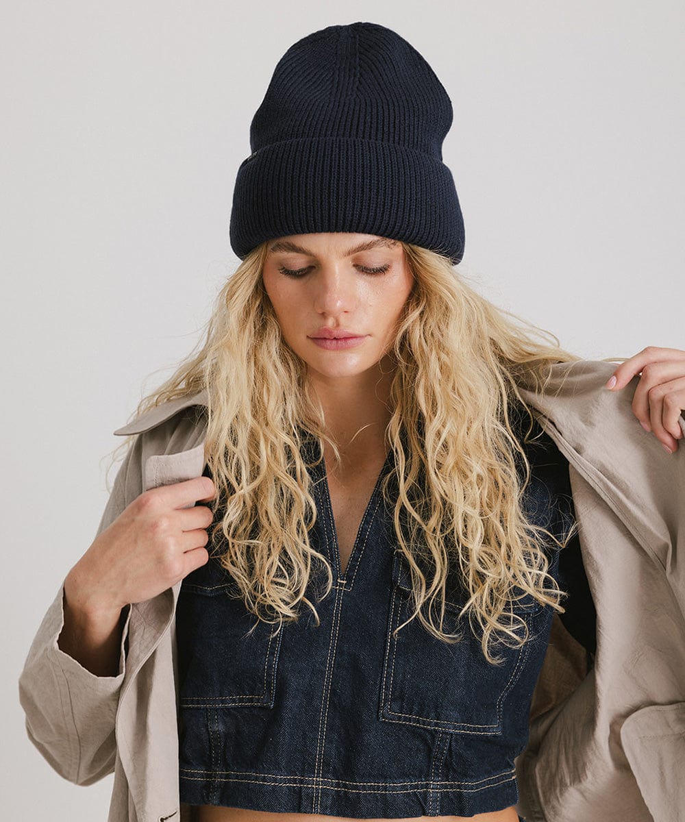 Woman wearing a navy oversized knit beanie and a denim top with a coat against a plain background #color_navy