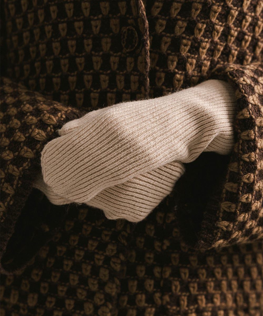 Close-up of a beige knitted glove inside a textured brown coat pocket. #color_taupe