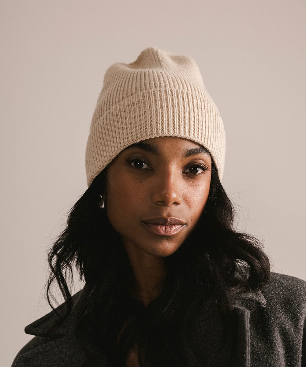 Woman wearing a beige knit beanie against a plain background #color_taupe