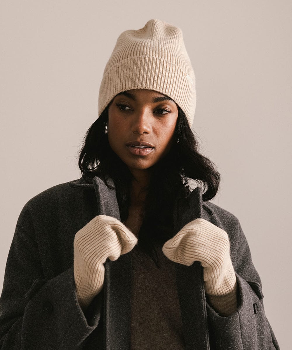 Person wearing a beige knit beanie and gloves against a neutral background #color_taupe