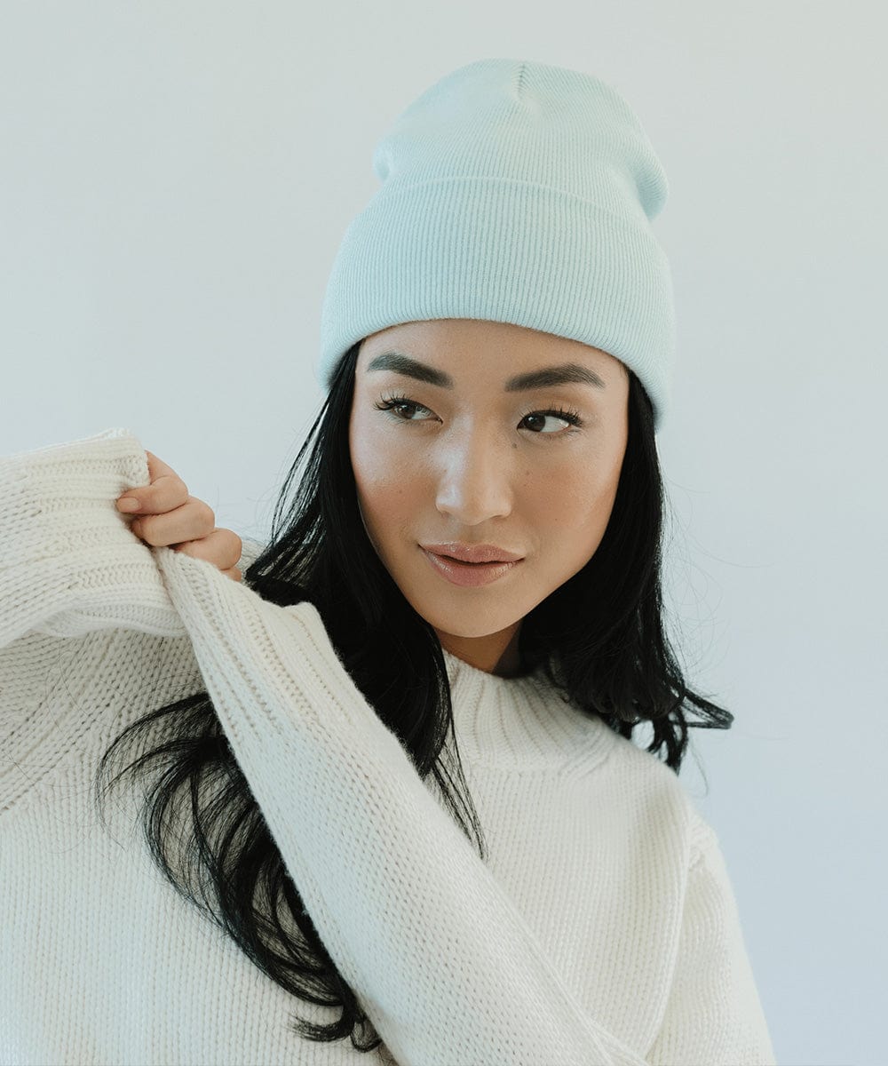 Woman wearing a sky blue beanie and a white sweater, posing against a plain background #color_sky blue