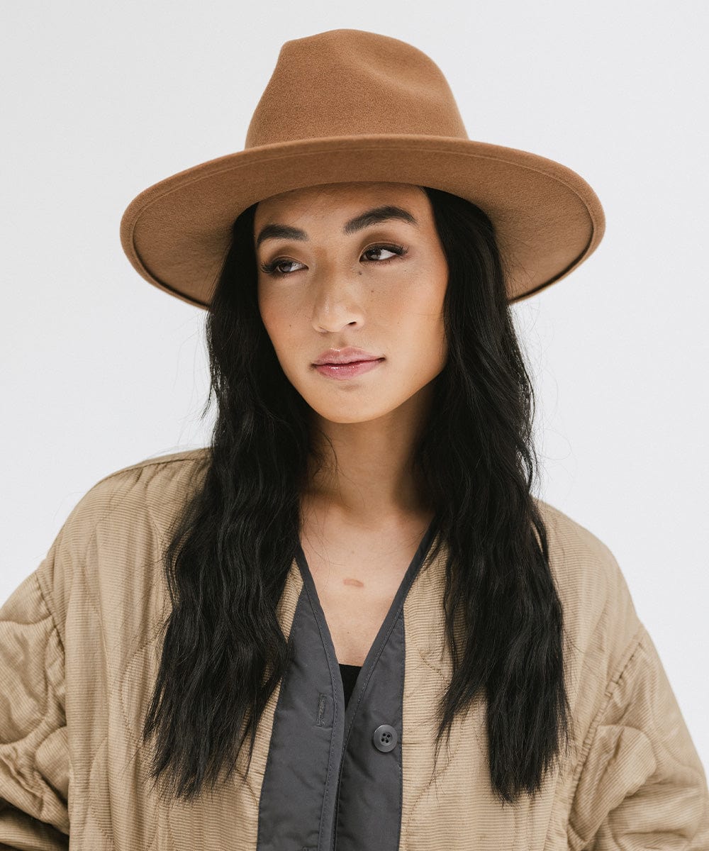 Woman wearing a brown fedora hat and a beige jacket against a plain background #color_brown