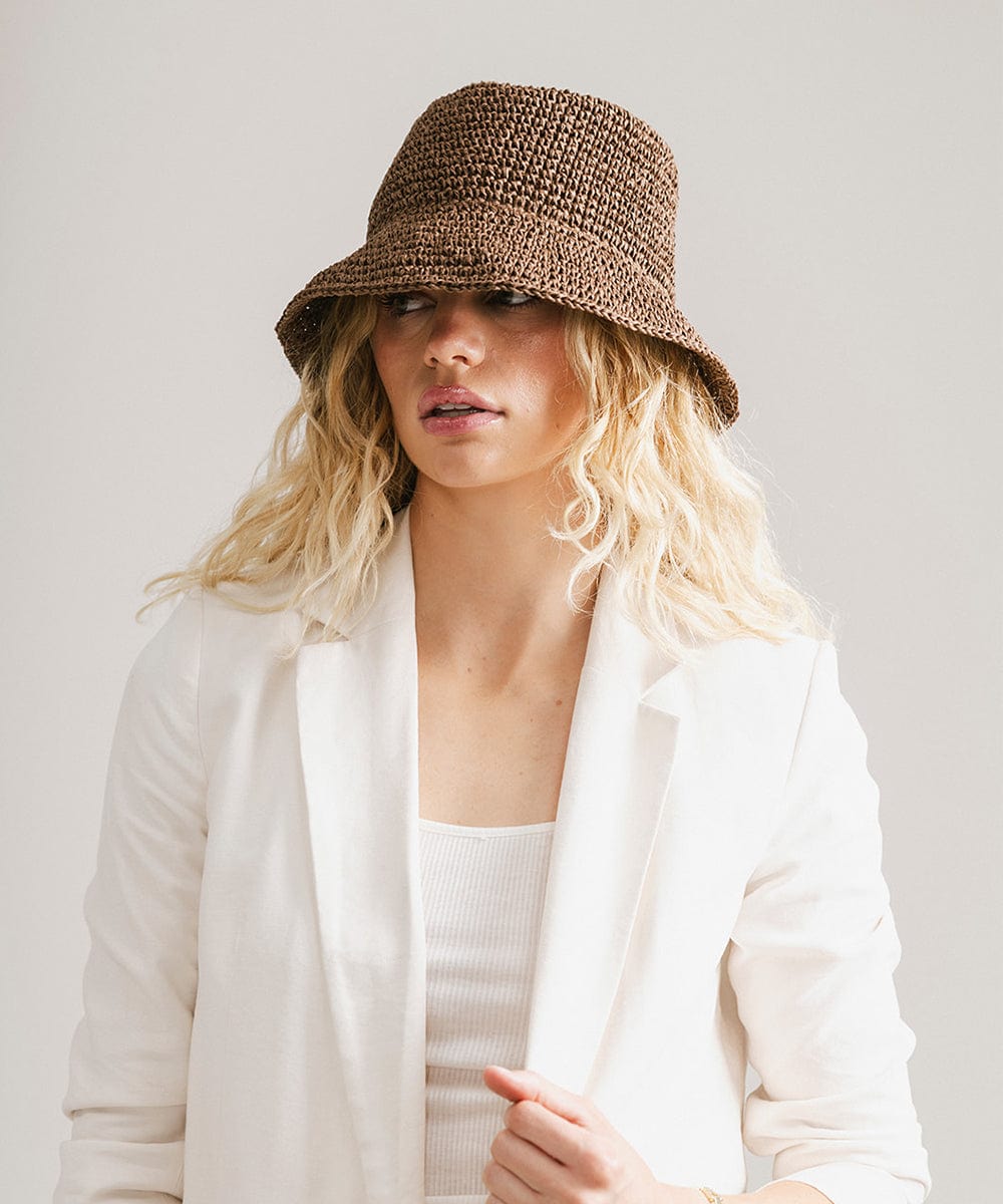 Woman wearing a chocolate colored bucket hat and white blazer against a plain background #color_chocolate