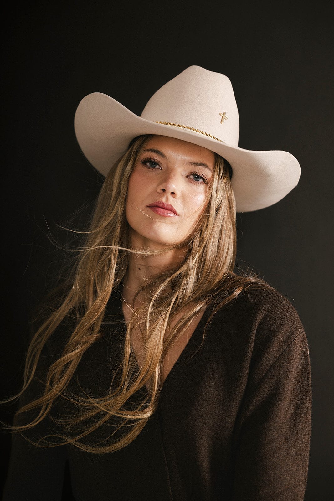 Woman wearing a beige cowboy hat against a black background #color_gold