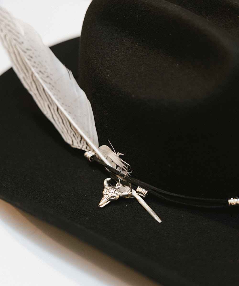 Black hat with a feather and silver decorative element on a white background