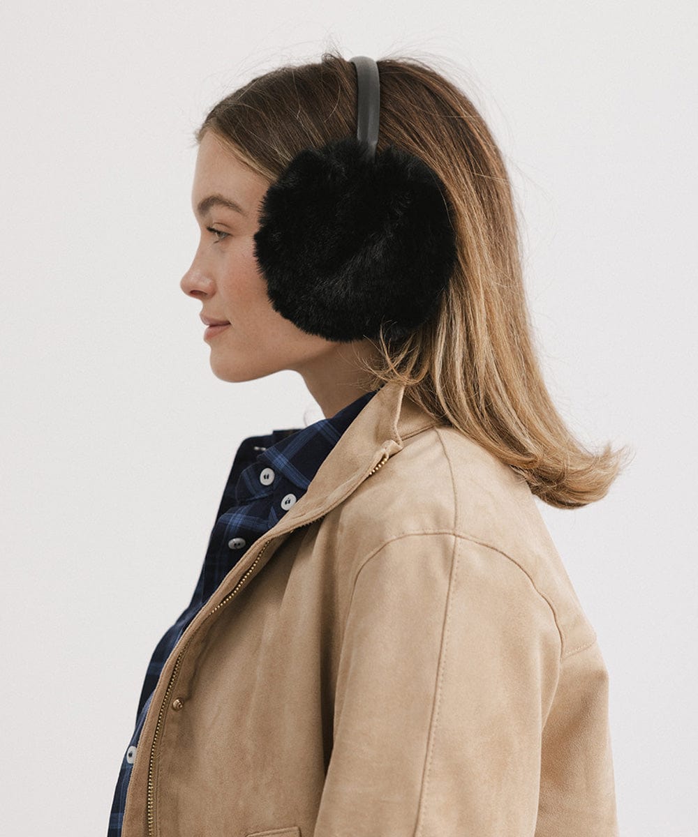 Woman wearing black fur ear muffs and a beige jacket, facing sideways against a plain background #color_black