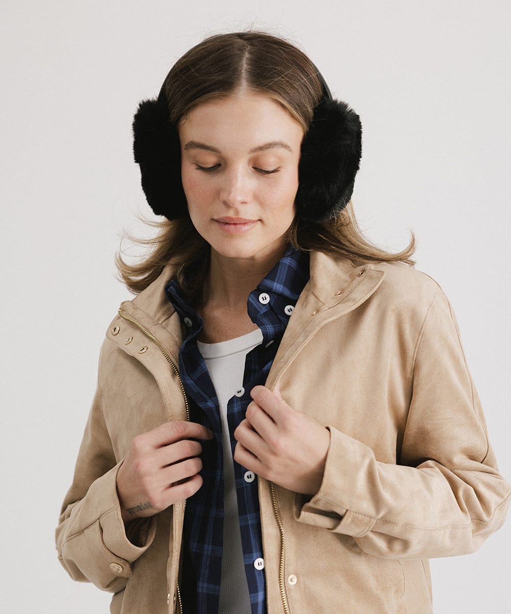 Woman wearing black fur ear muffs and a beige jacket against a plain background #color_black