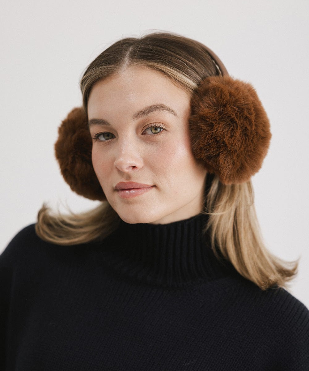 Woman wearing brown fur ear muffs and a black sweater against a plain background #color_brown