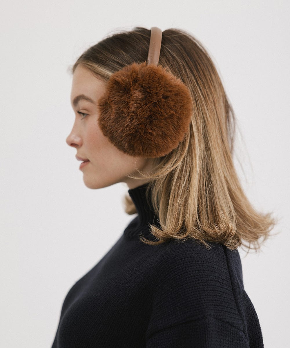 Woman wearing brown fur ear muffs and a black sweater, facing sideways against a plain background #color_brown