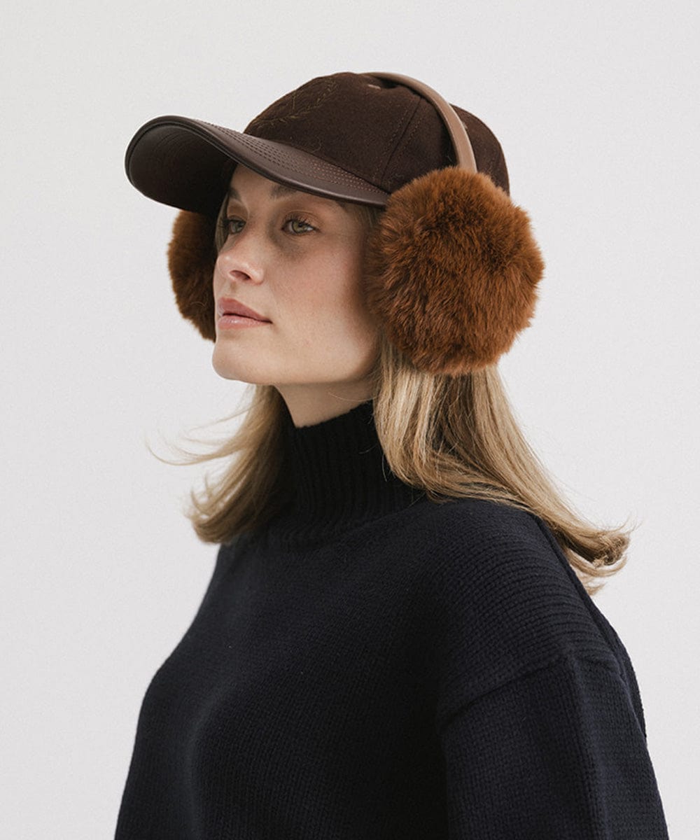 Woman wearing brown fur ear muffs and a black sweater, posing sideways against a plain background #color_brown