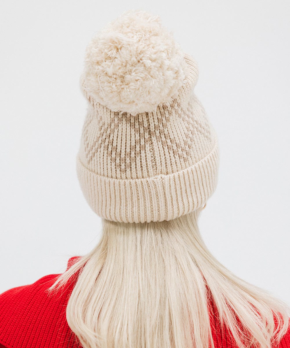 Woman wearing a cream knit beanie with a pom-pom and a red jacket, facing behind against a plain background #color_cream