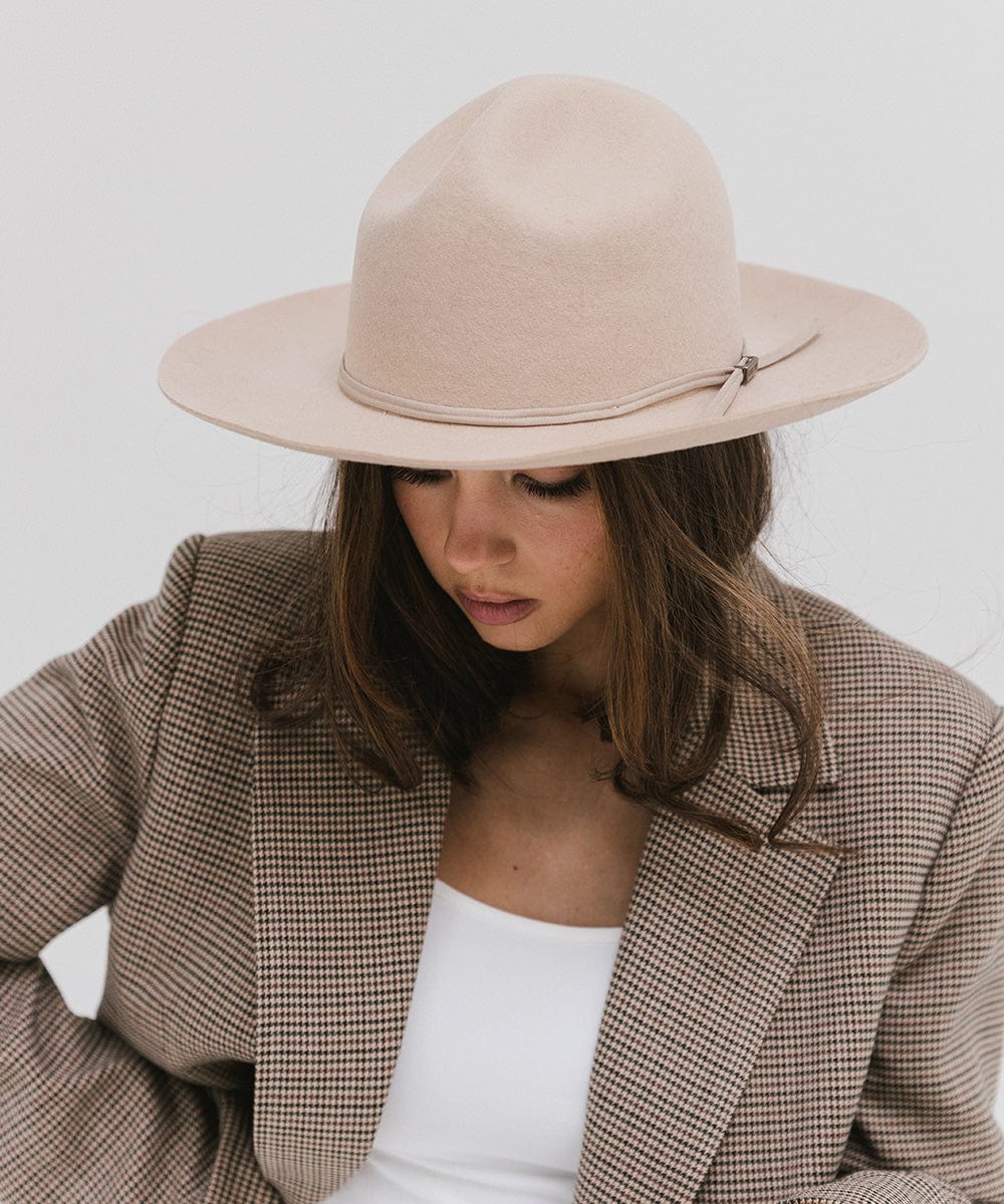 Woman wearing a cream fedora hat with a hat band and a white top with a checkered coat, looking down against a plain background #color_cream