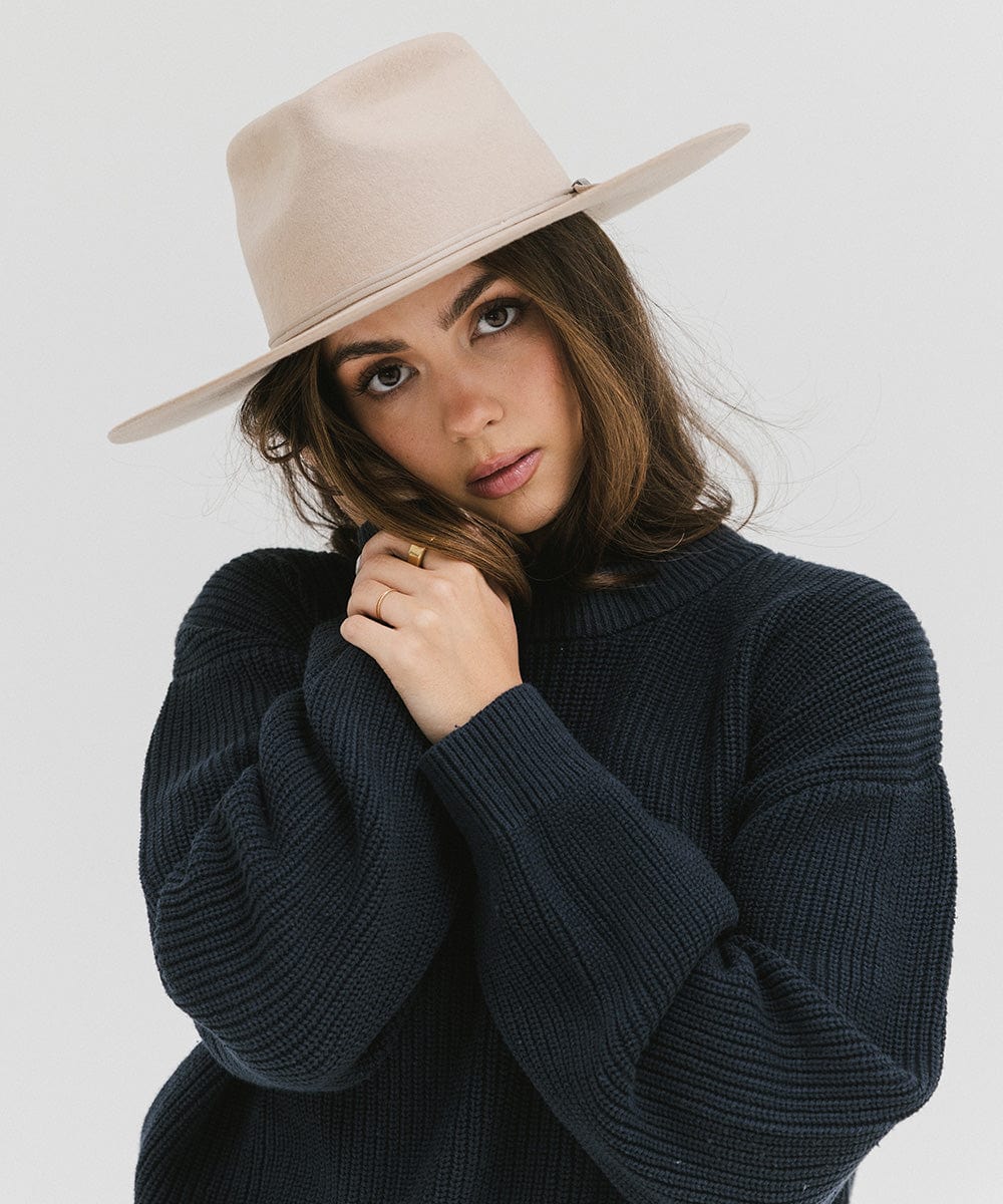 Woman wearing a cream Emery Teardrop Fedora Hat and a dark blue sweatshirt against a plain background #color_cream