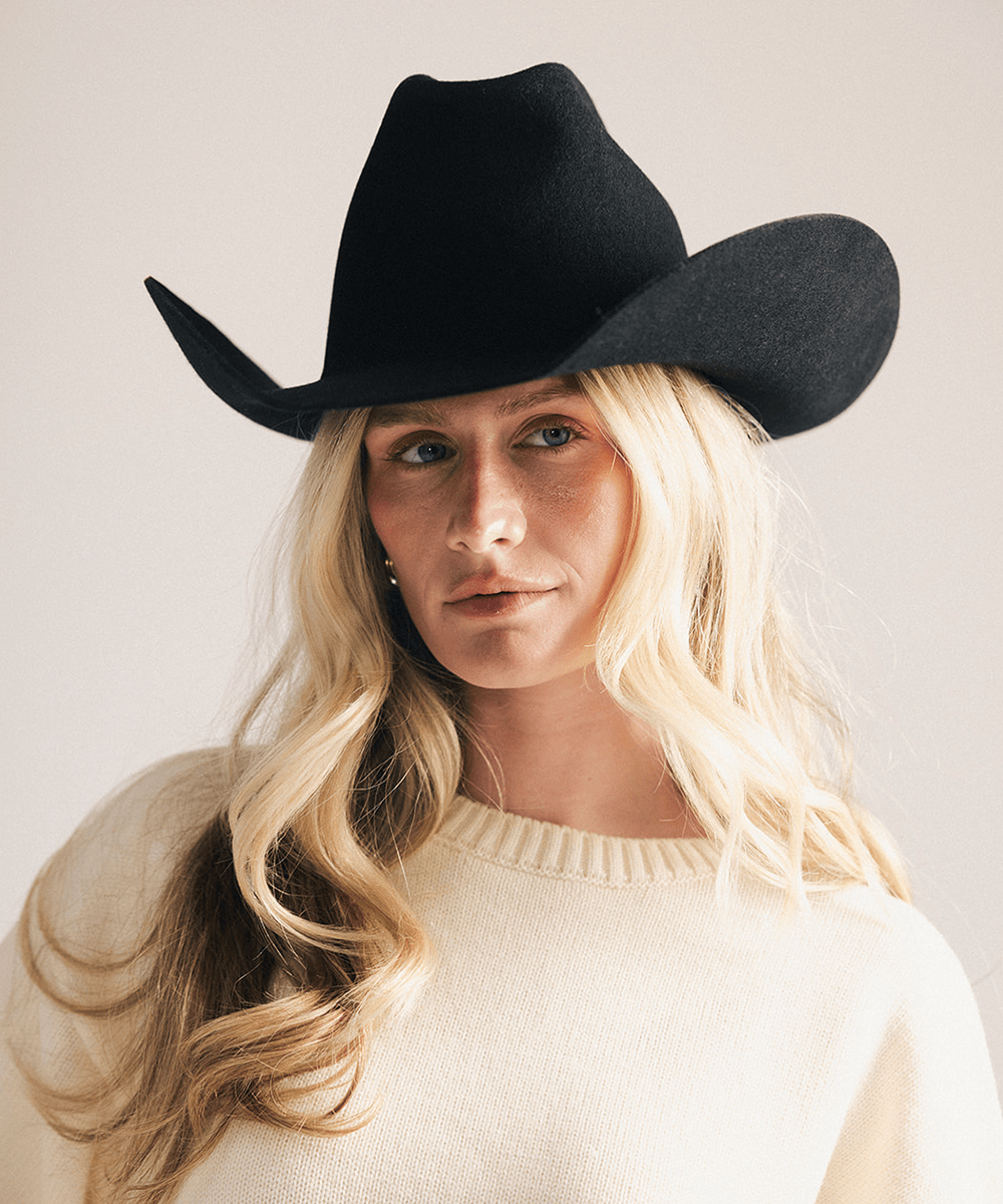 Woman wearing a black cowboy hat and cream sweater against a plain background #color_black