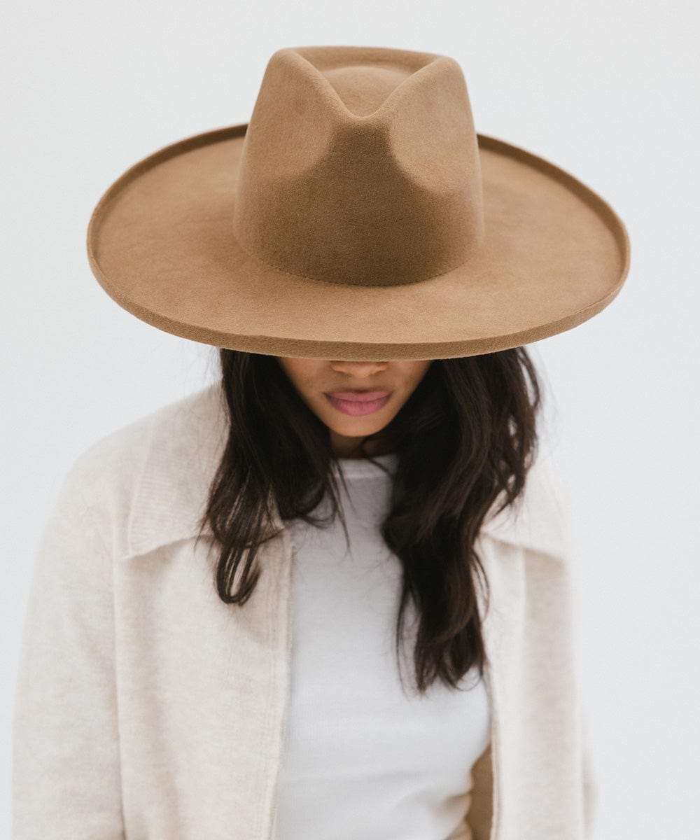 Woman wearing a brown pencil brim fedora hat with a wide brim and a cream jacket against a white background #color_brown