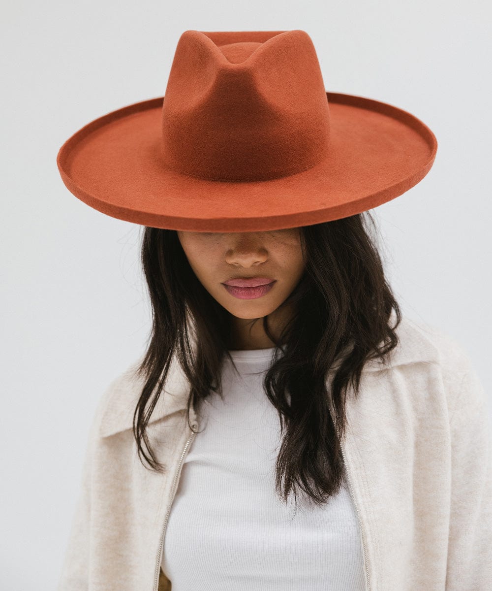 Woman wearing a clay colored pencil brim fedora hat with a wide brim and a cream jacket against a white background #color_clay