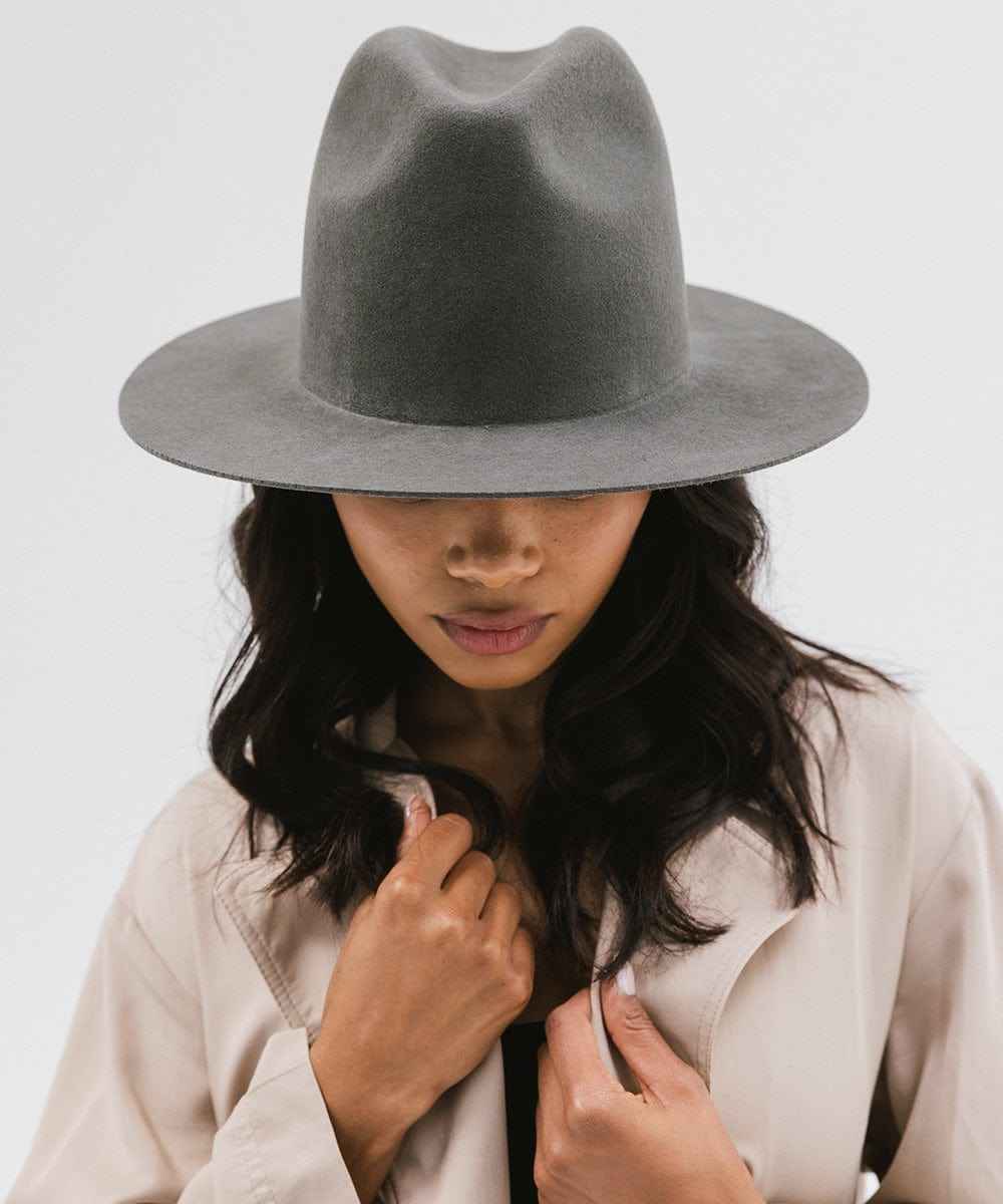 Person wearing a dark grey fedora and beige coat on a white background #color_dark grey